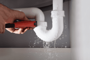 a leaking pipe with a hand holding a wrench to stop the leak